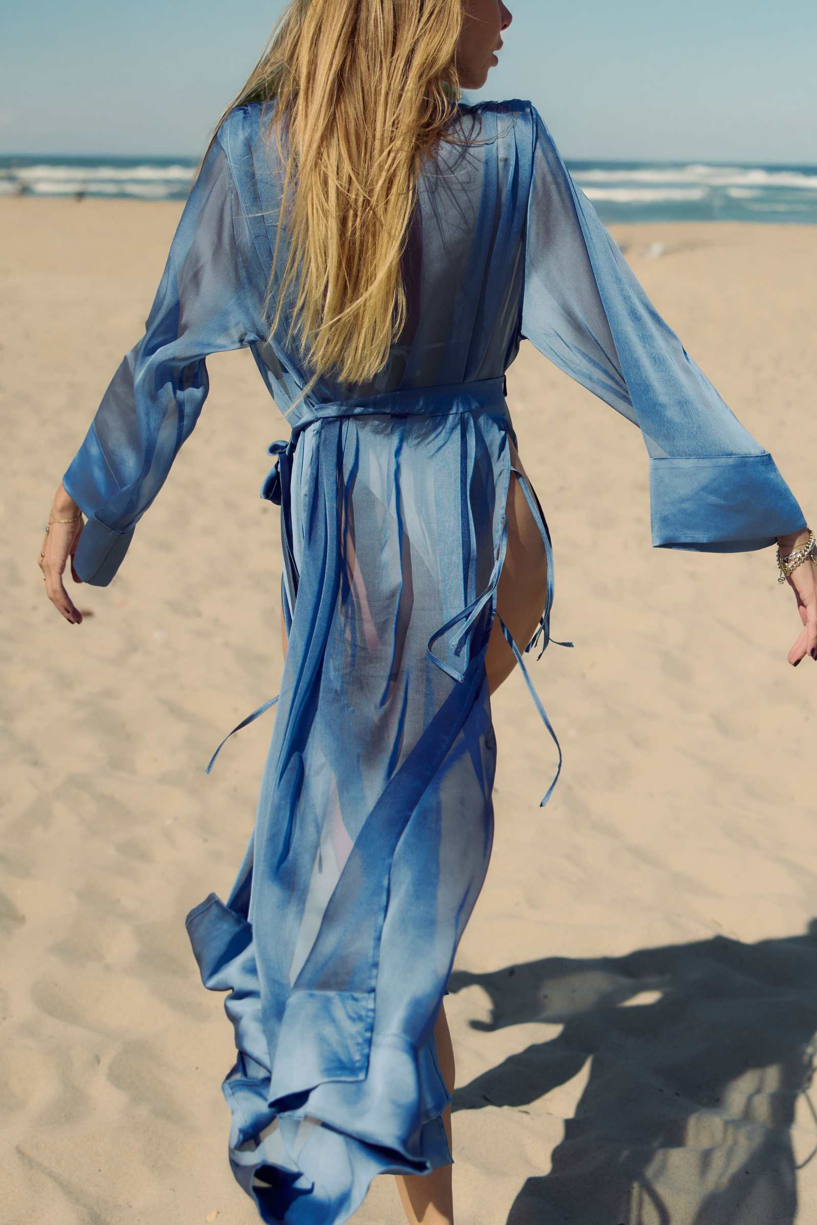 Woman in a blue dress walking on a sandy beach with ocean view