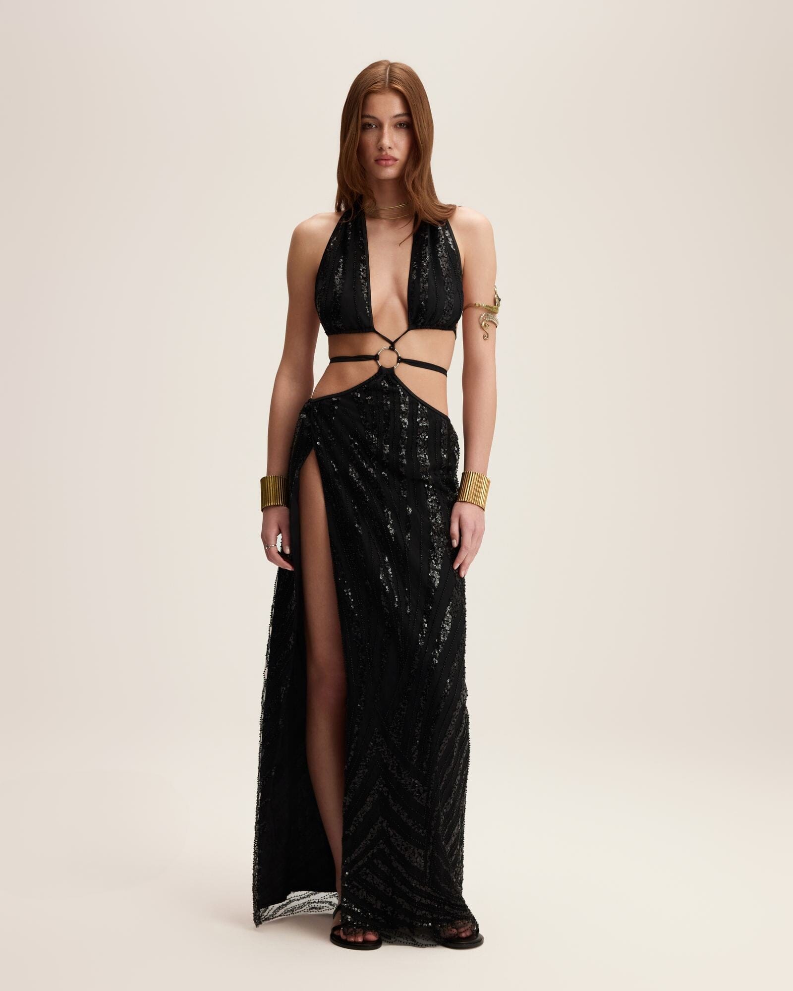 Model wearing a black sequin outfit with cut-out design on a beige background
