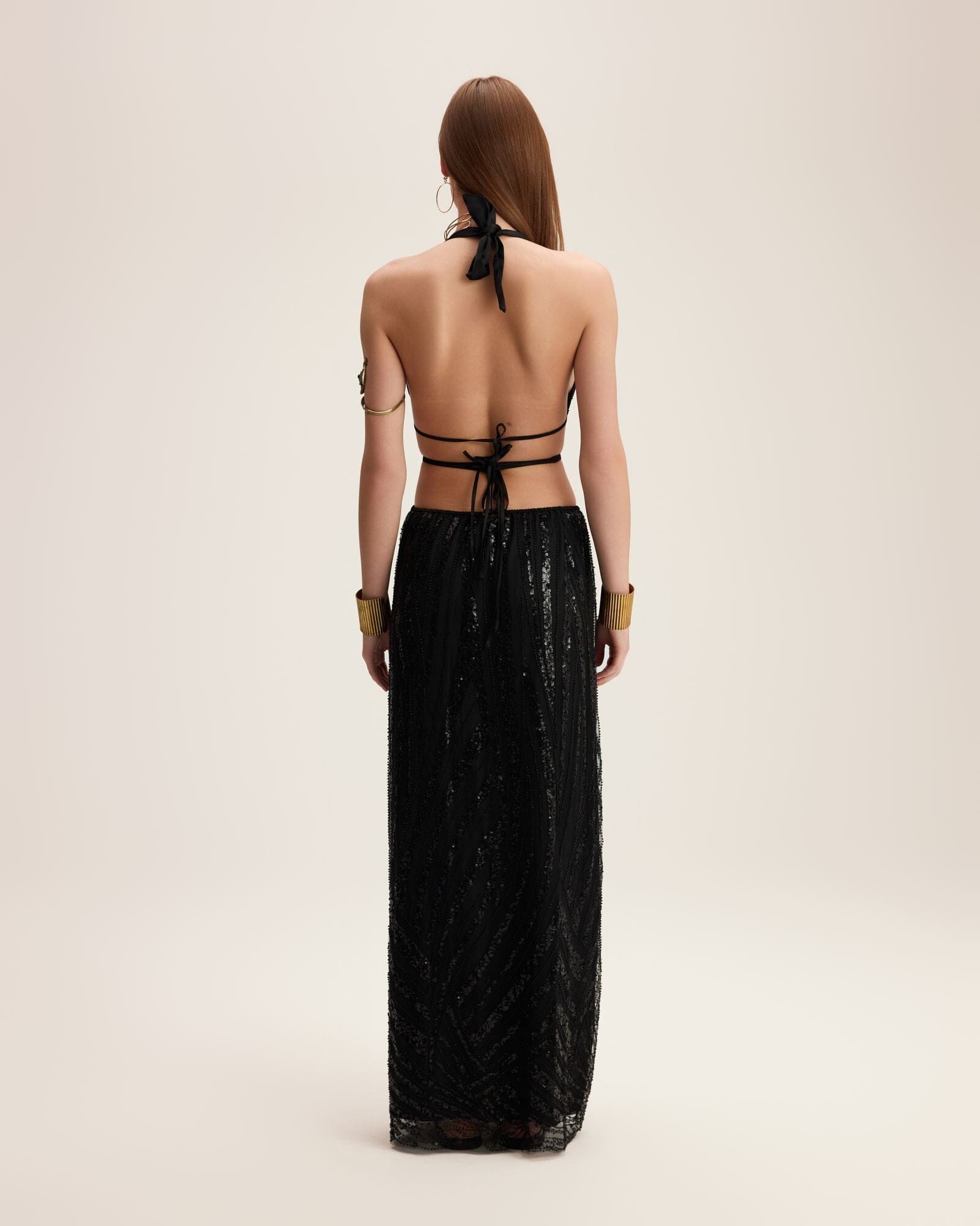 Woman wearing a black dress with a halter neck and long skirt on a beige background