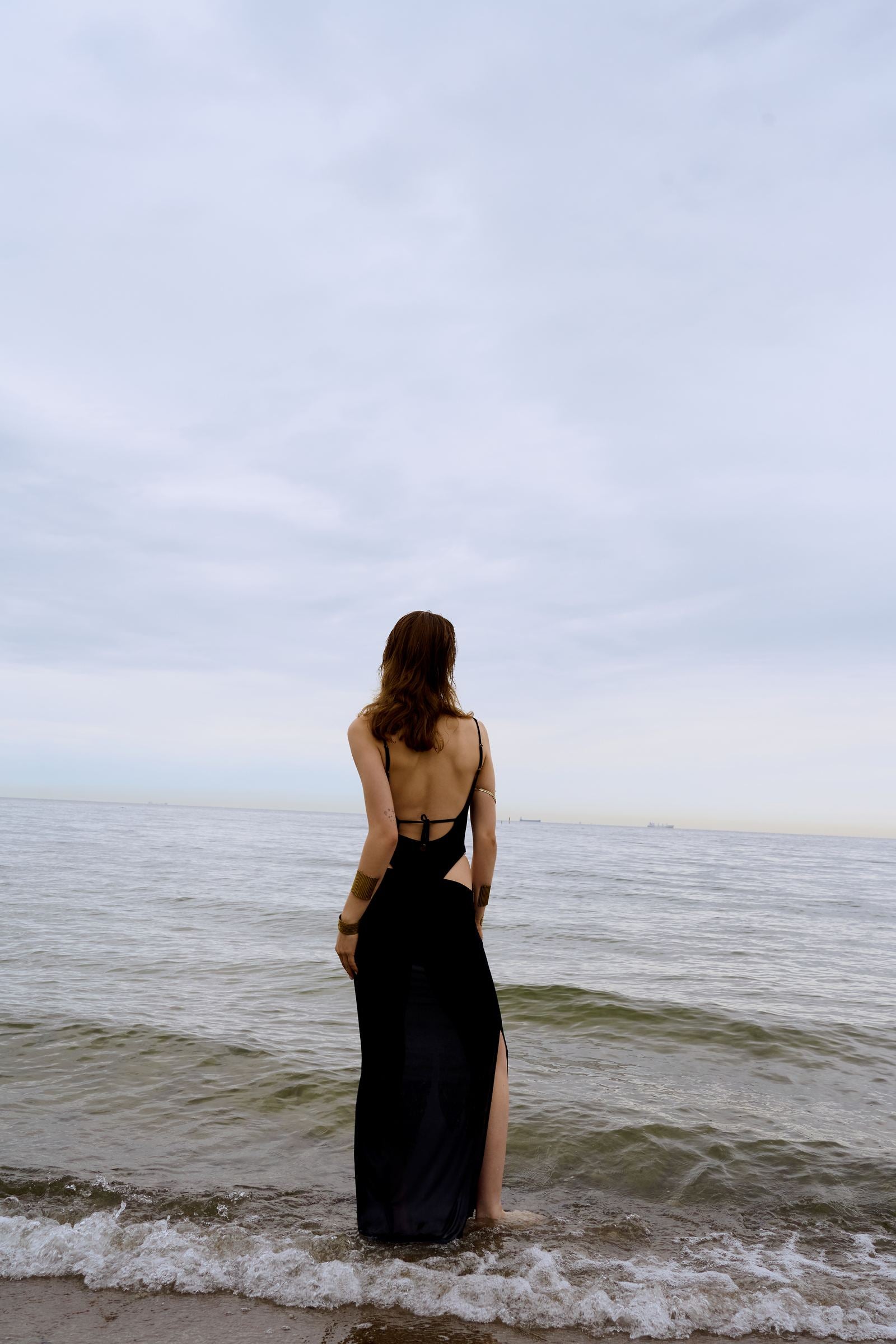 Woman in a black dress standing in shallow water at the beach