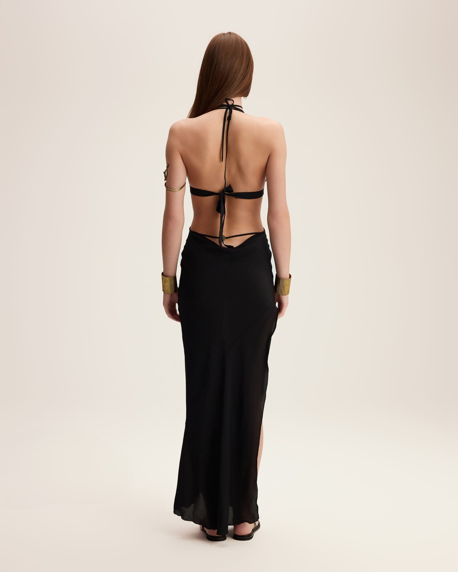 Woman wearing a black halter neck dress with cut-out design on a beige background