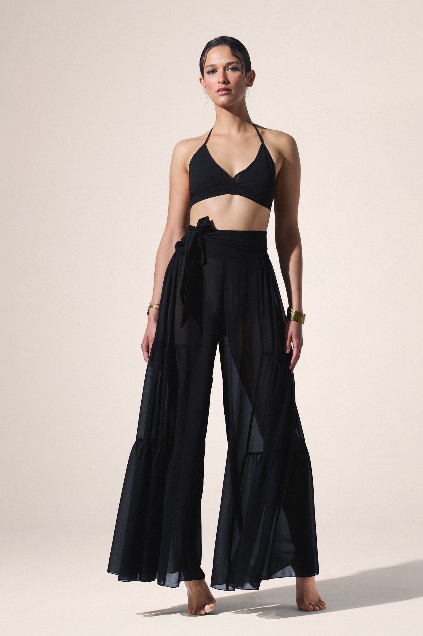Woman wearing a black outfit with wide-leg pants and a top on a beige background