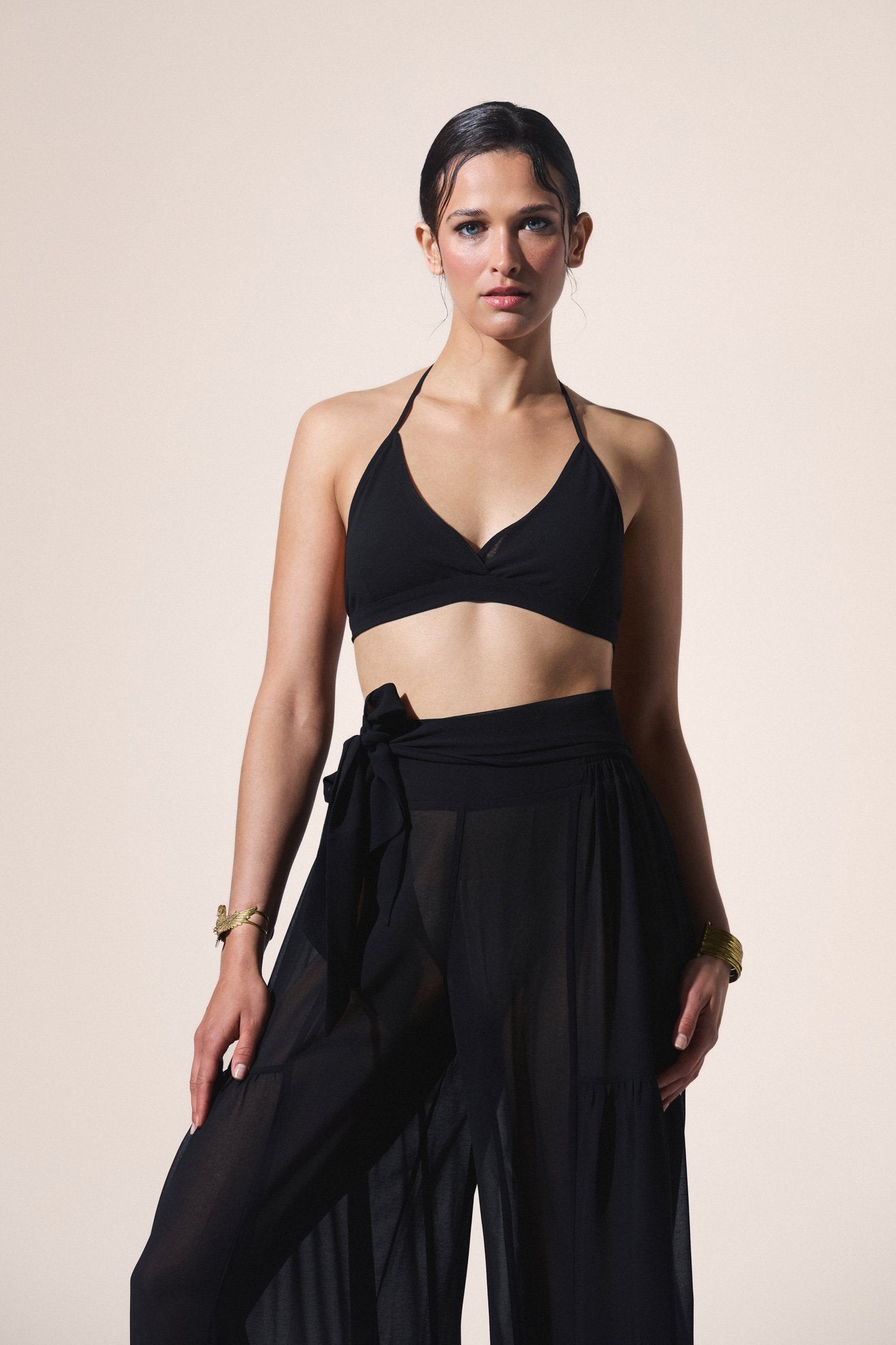 Woman wearing a black halter top and flowing black pants against a beige background