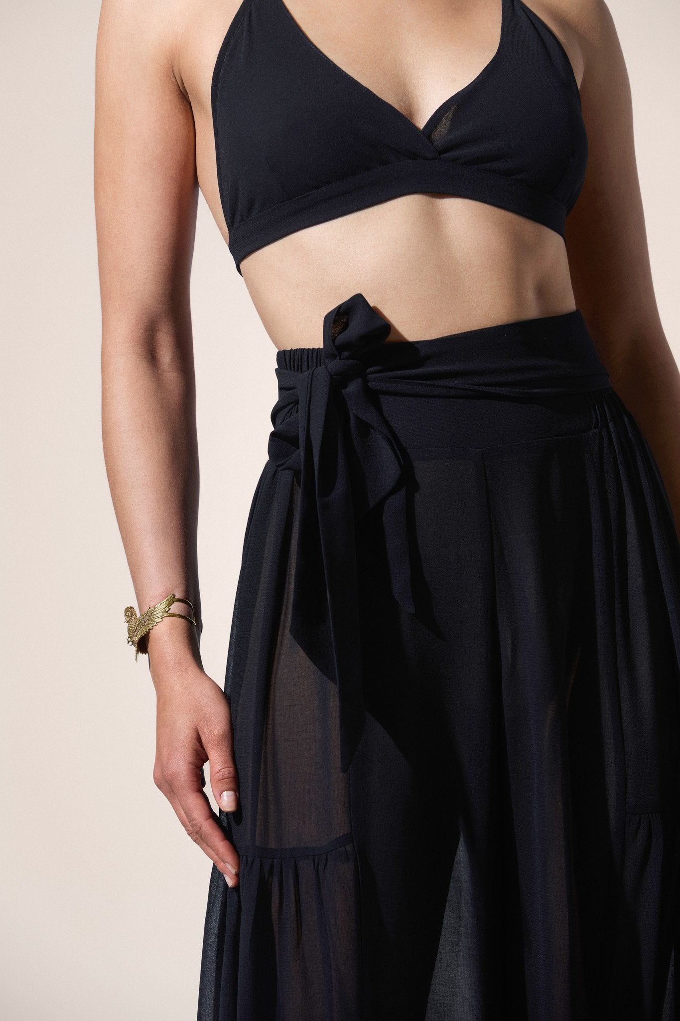 Person wearing a black bikini top and black skirt against a beige background