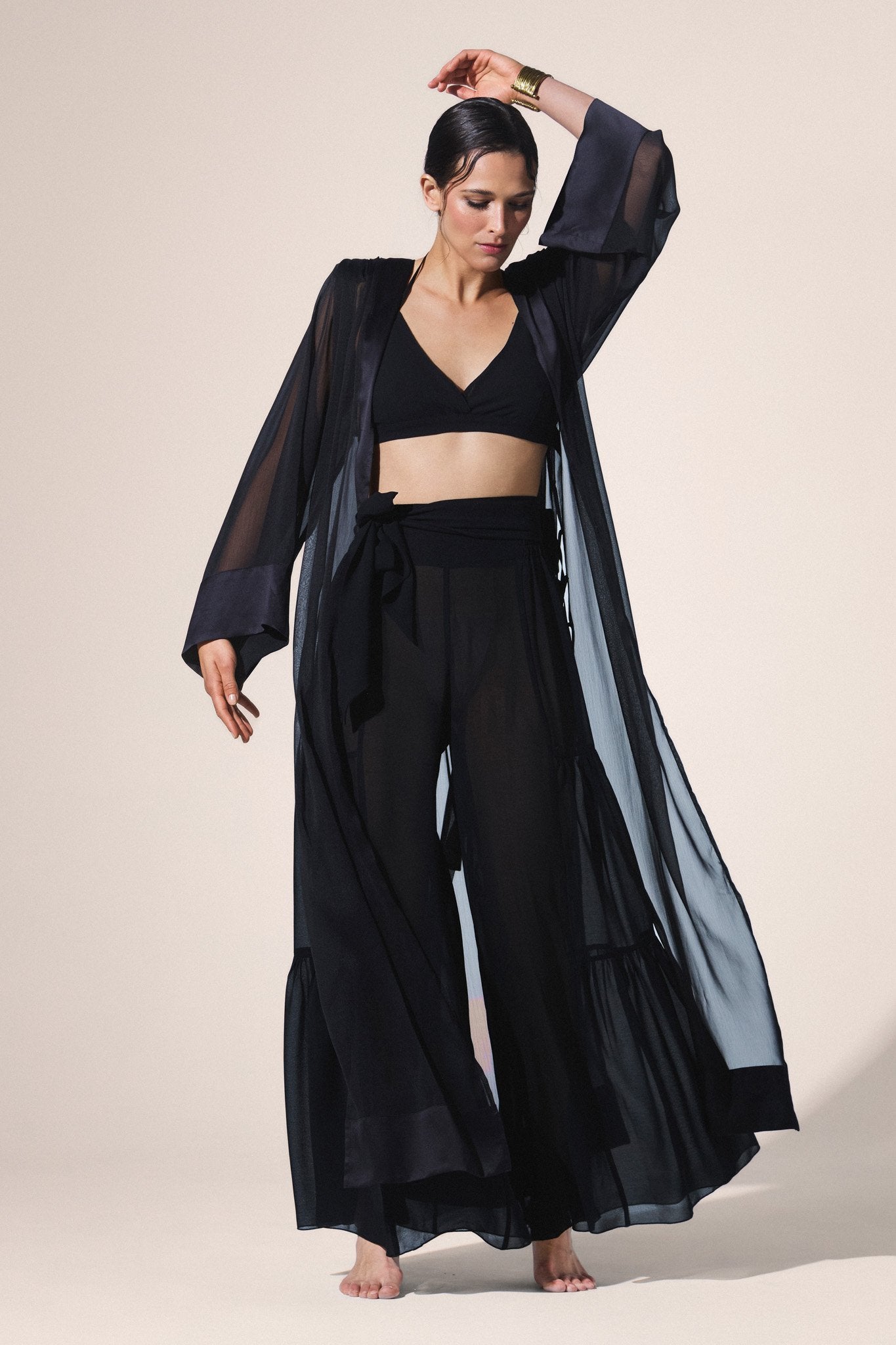 Woman wearing a black outfit with a long sheer jacket on a beige background