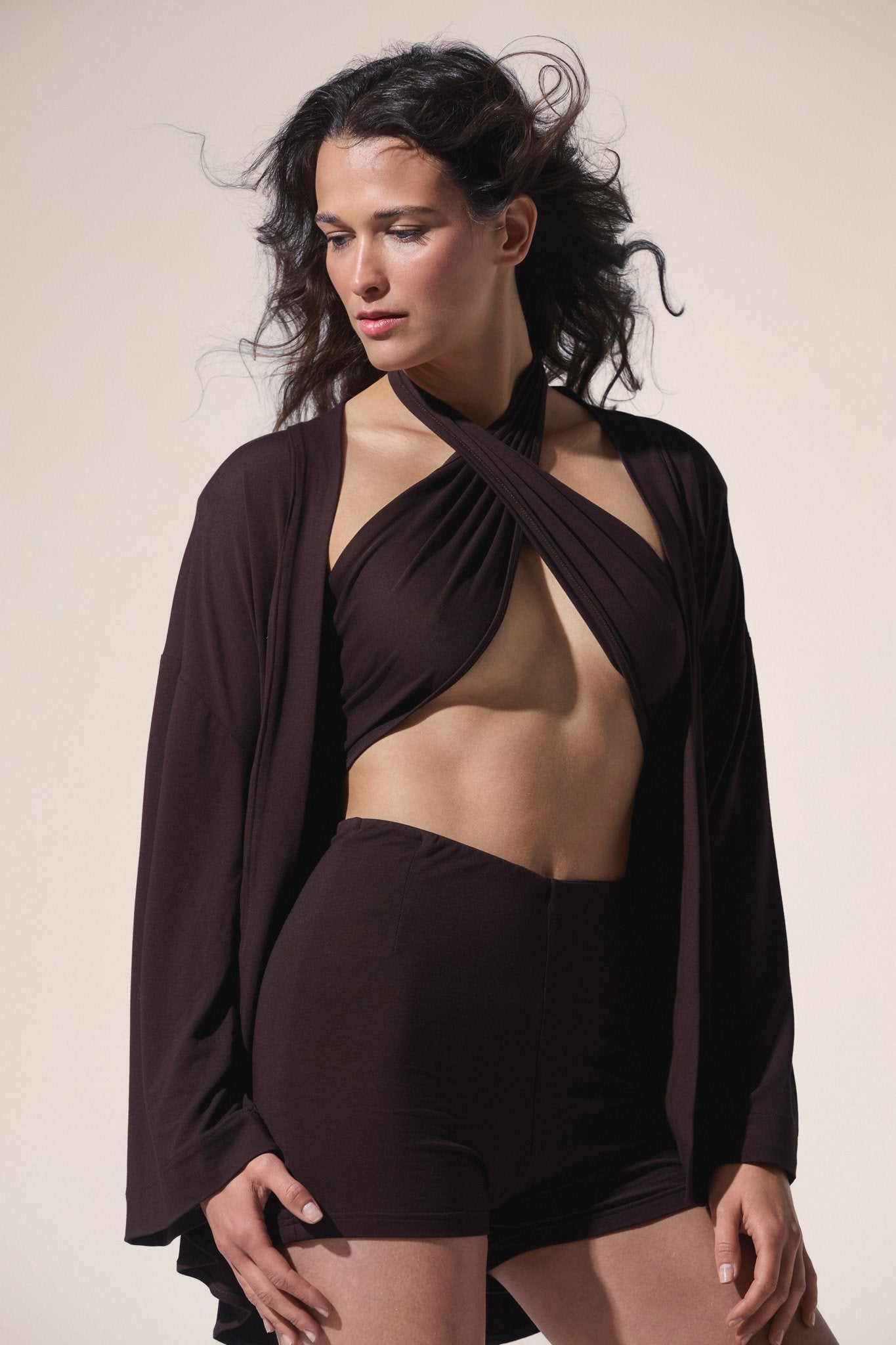 Woman wearing a brown outfit with a draped top and shorts on a beige background