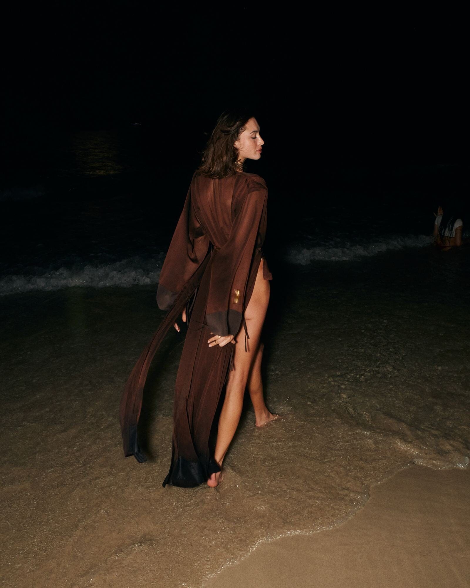 Person in a dark outfit standing on a beach at night