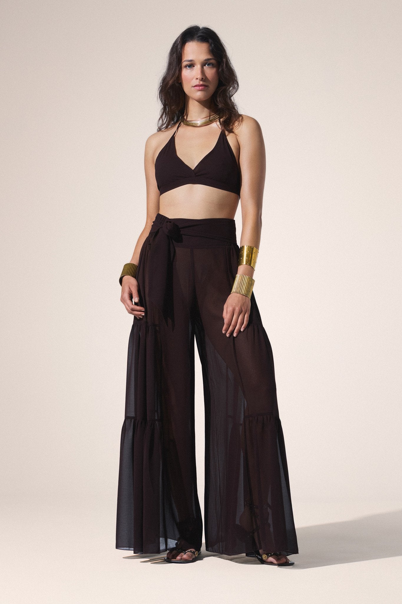 Woman wearing a brown outfit with wide-leg pants and a halter top on a beige background