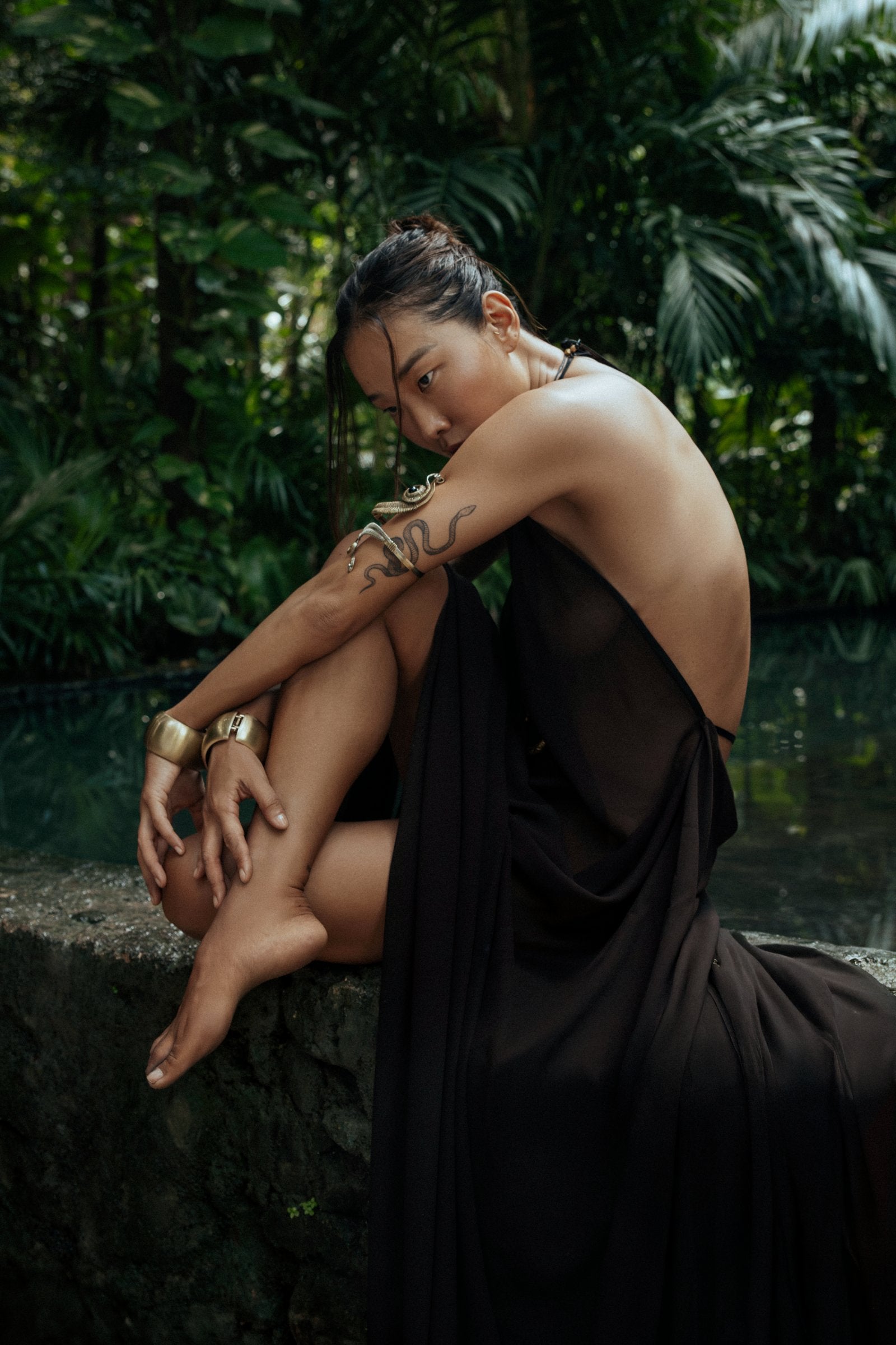 Woman in a brown dress sitting by a pool with greenery in the background