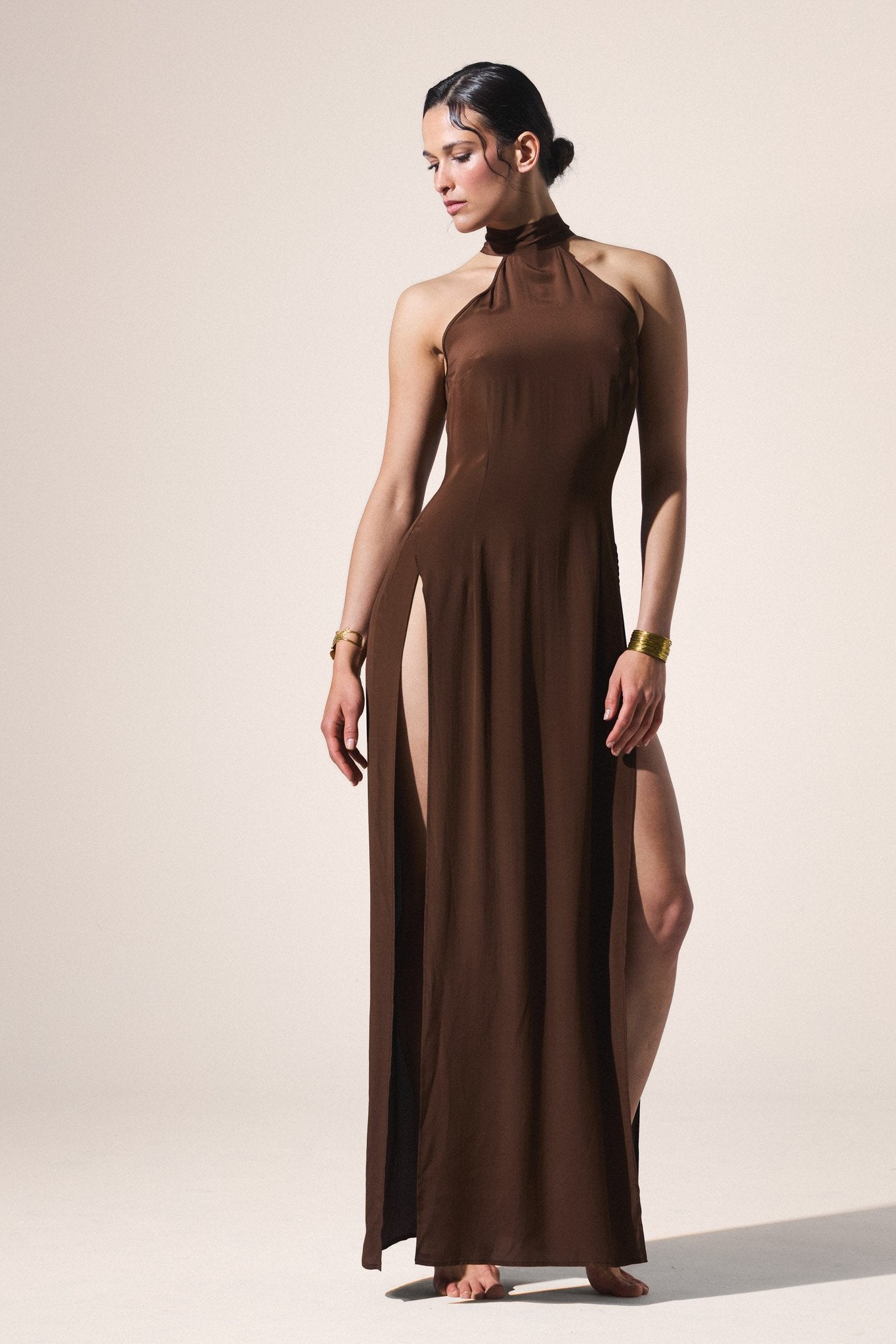 Woman wearing a brown halter neck dress with a slit on a beige background