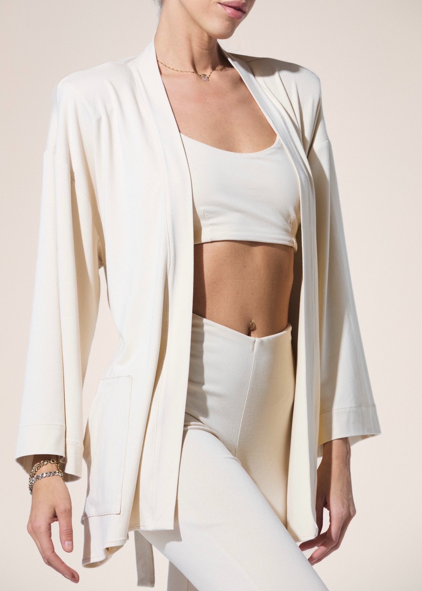Person wearing a white outfit with a matching cardigan on a beige background