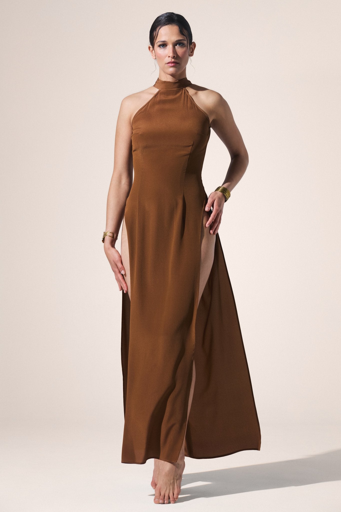 Woman wearing a gold halter neck dress with a slit on a beige background