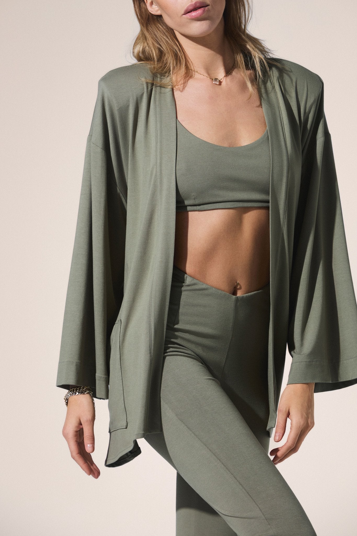 Woman wearing a green athletic outfit with a matching kimono on a beige background
