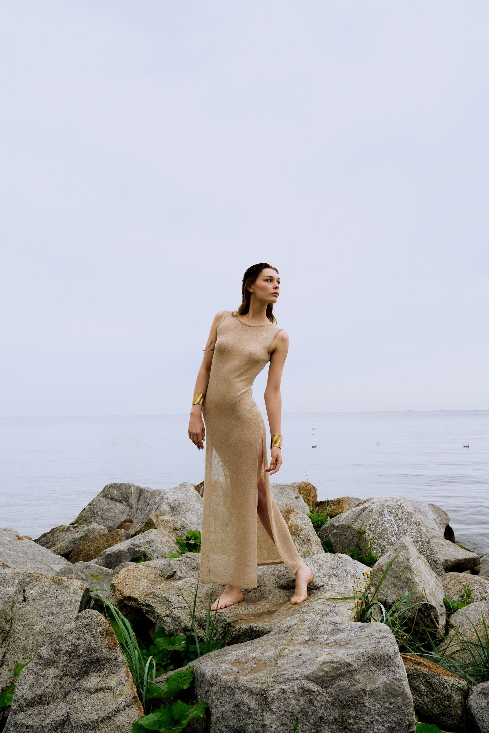 Woman in a beige dress standing on rocks by the water