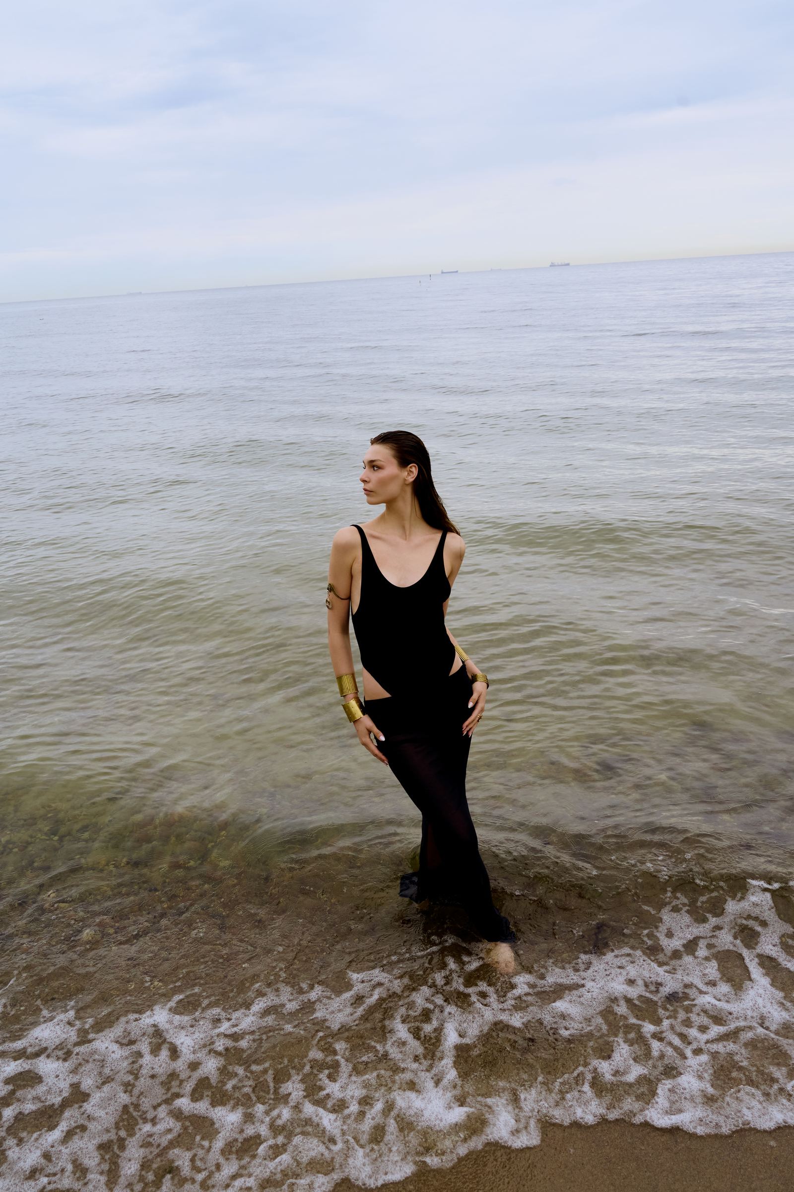 Woman in a black dress standing in shallow water on a beach