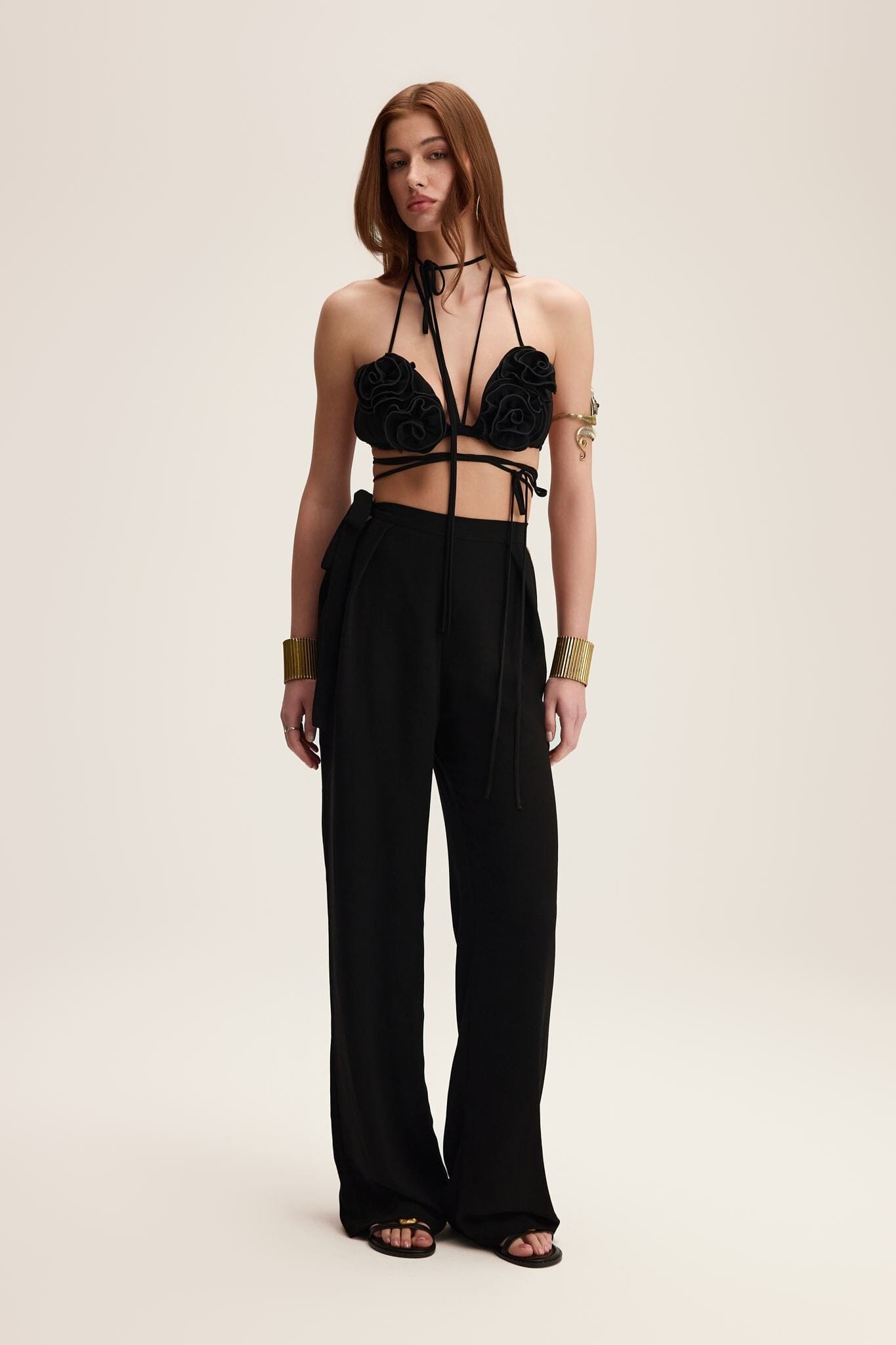 Woman wearing a black strappy top and high-waisted pants on a beige background