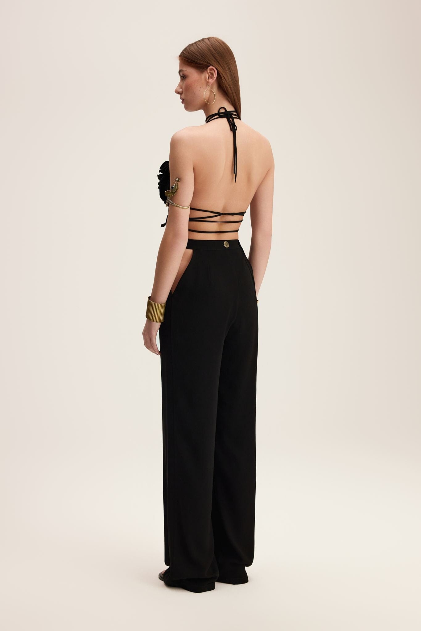 Woman wearing a black outfit with a lace-up back on a beige background