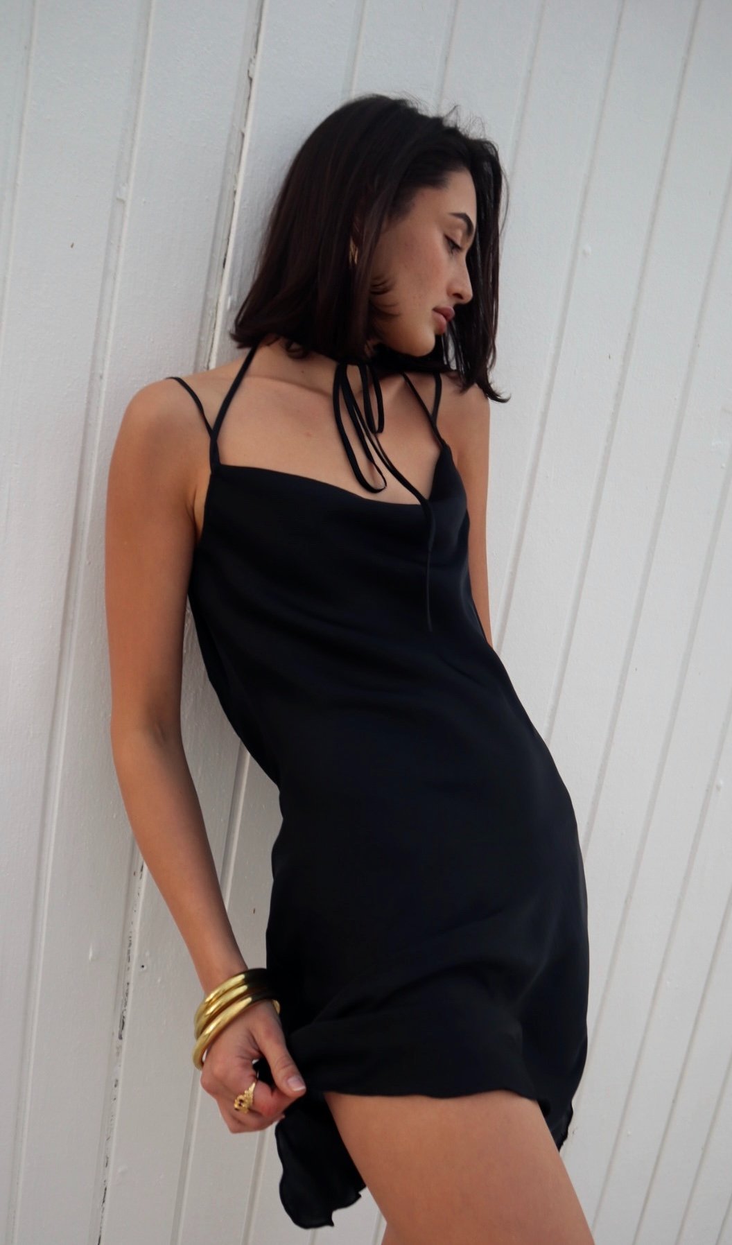 Woman wearing a black slip dress against a white wooden panel background