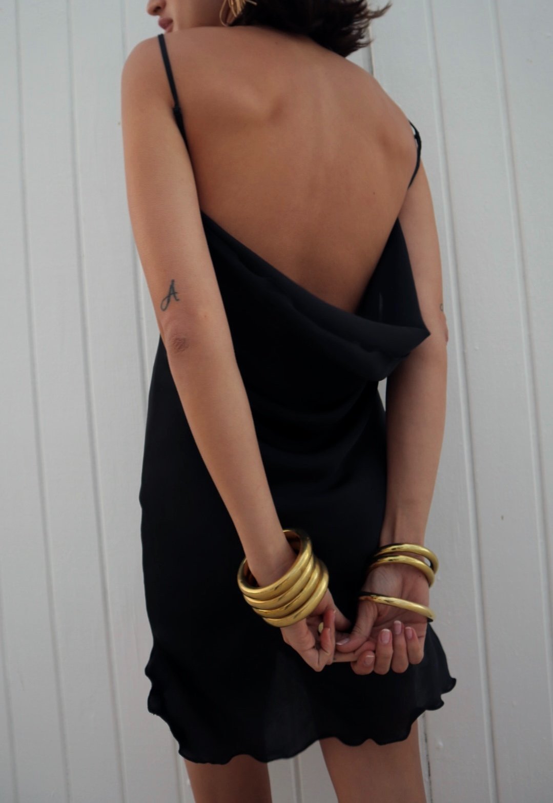 Person wearing a black dress with gold bracelets on a white background