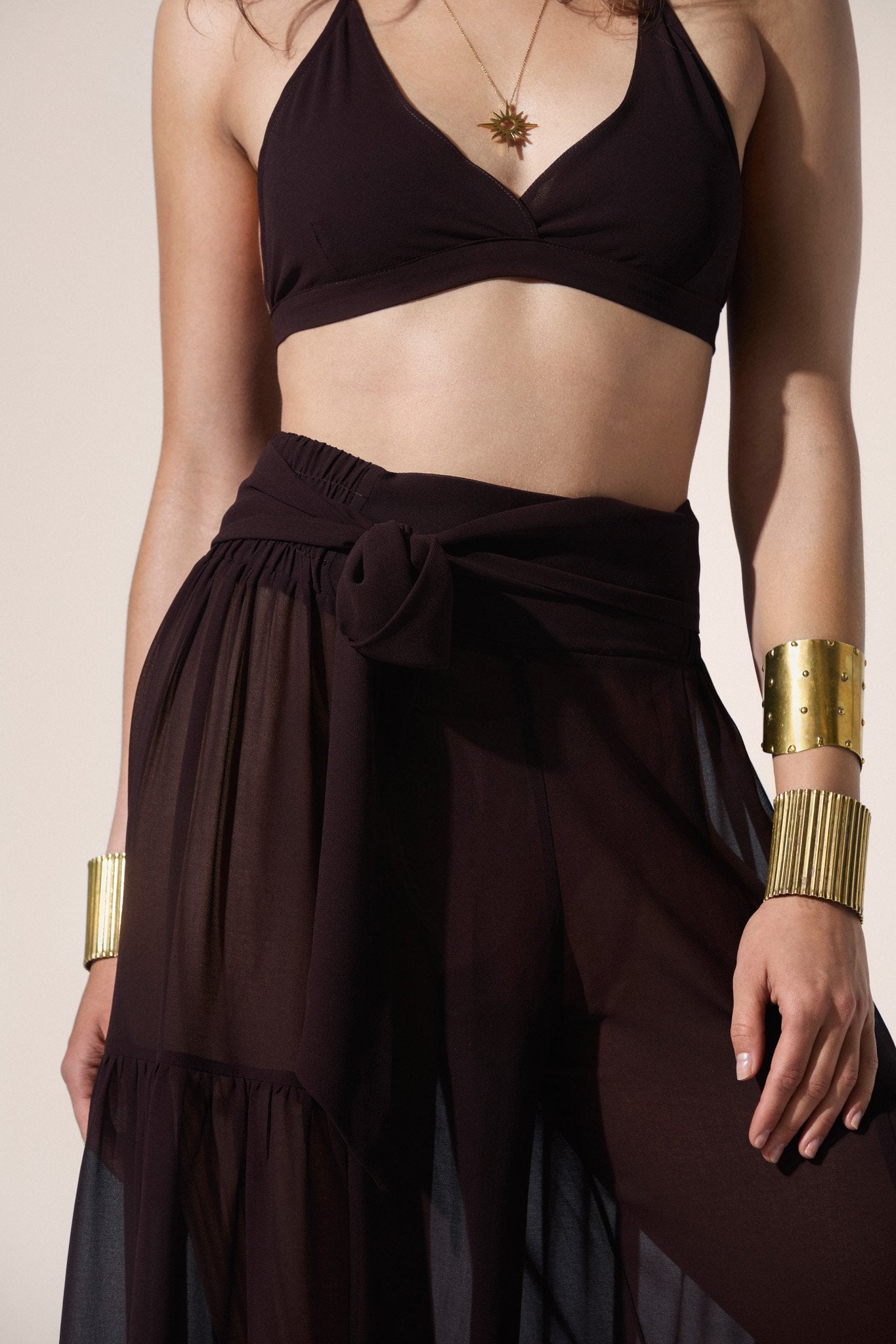 Woman wearing a brown two-piece outfit with gold accessories on a beige background