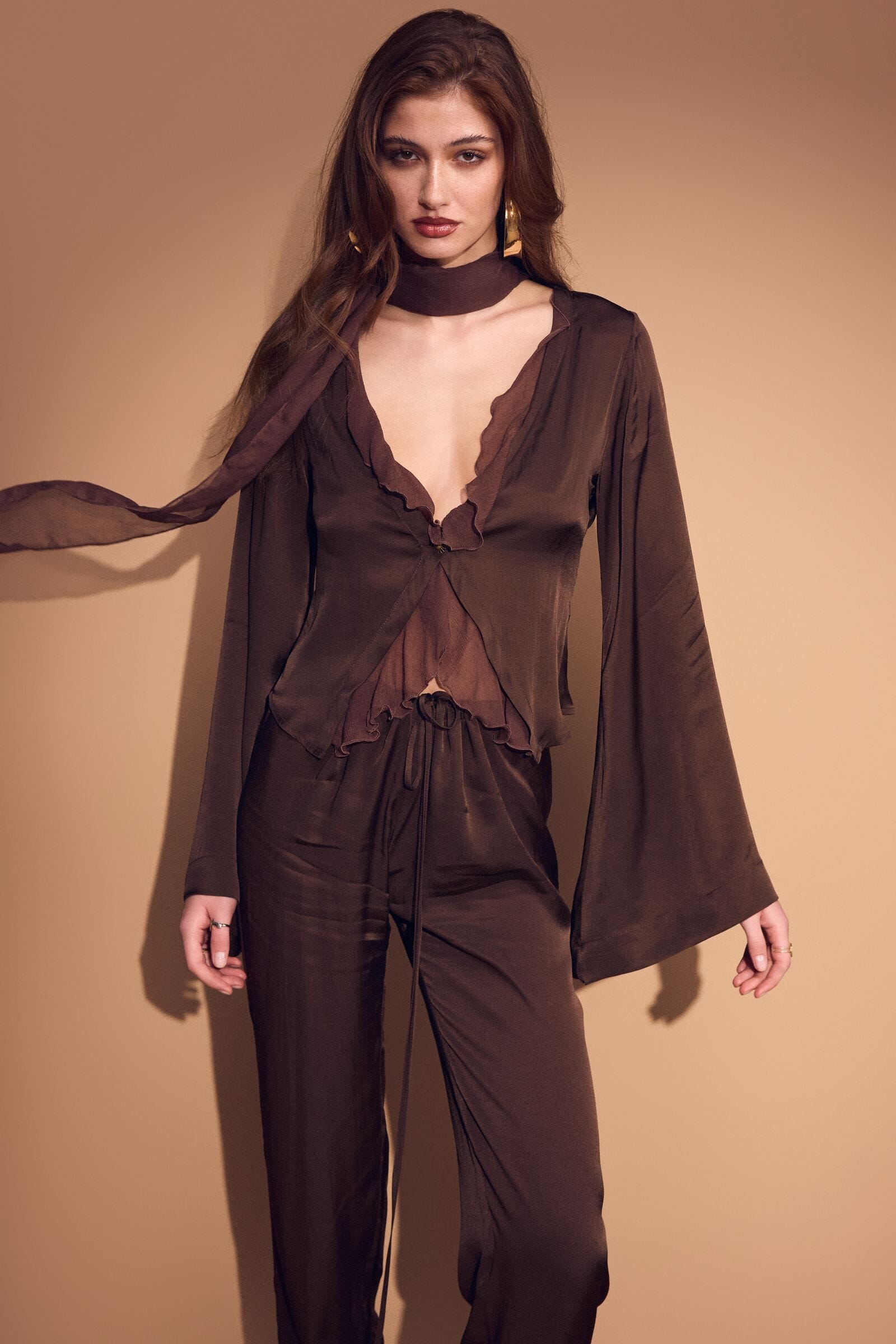 Woman wearing a brown outfit with a scarf against a beige background