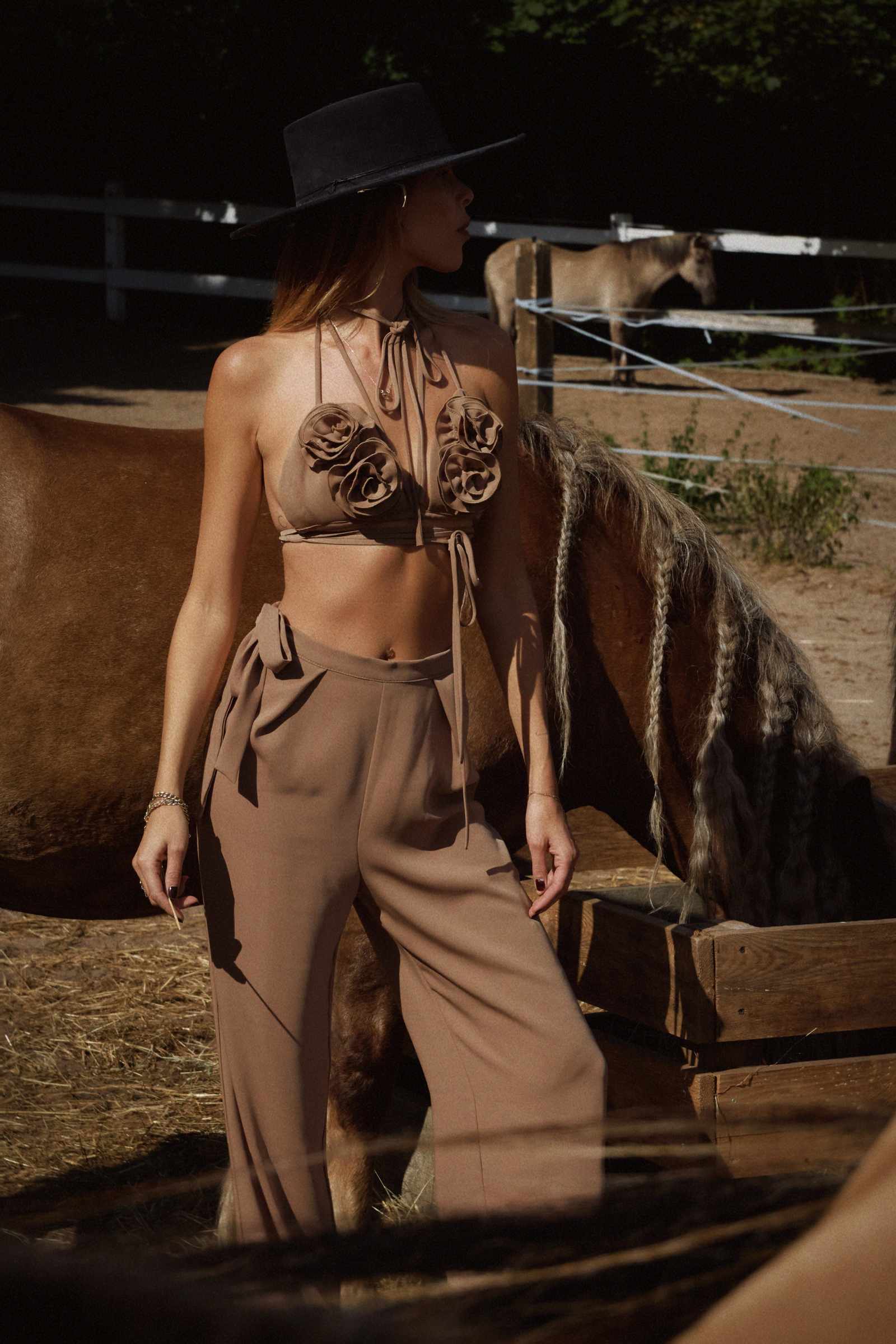 Woman in a cowboy hat and cappucino outfit standing next to a horse in a stable.