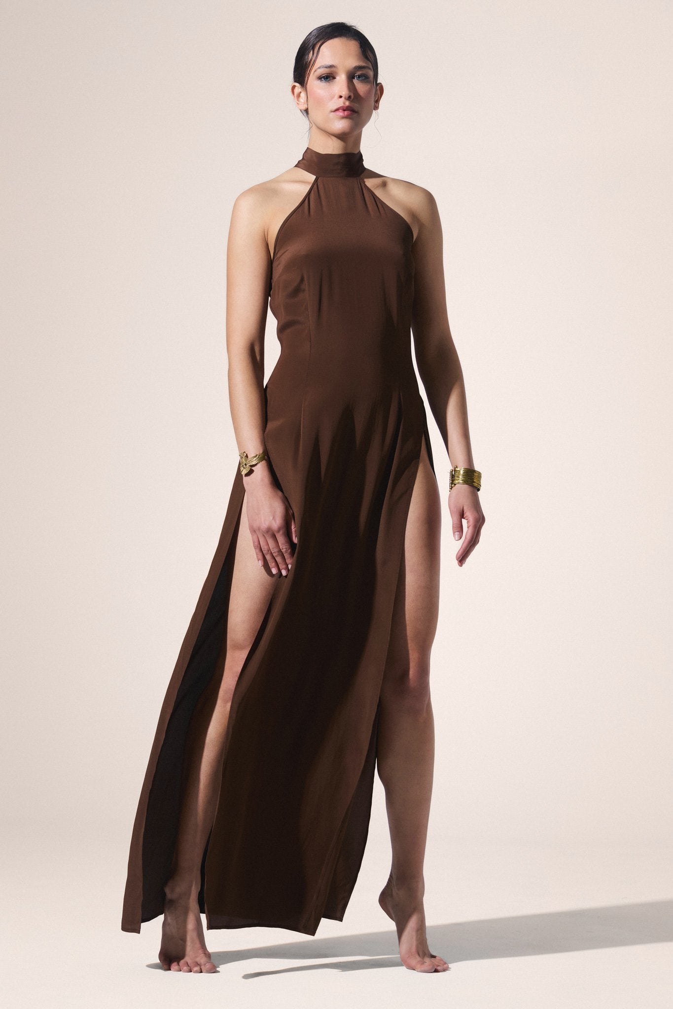Woman wearing a brown halter neck dress with a high slit on a beige background