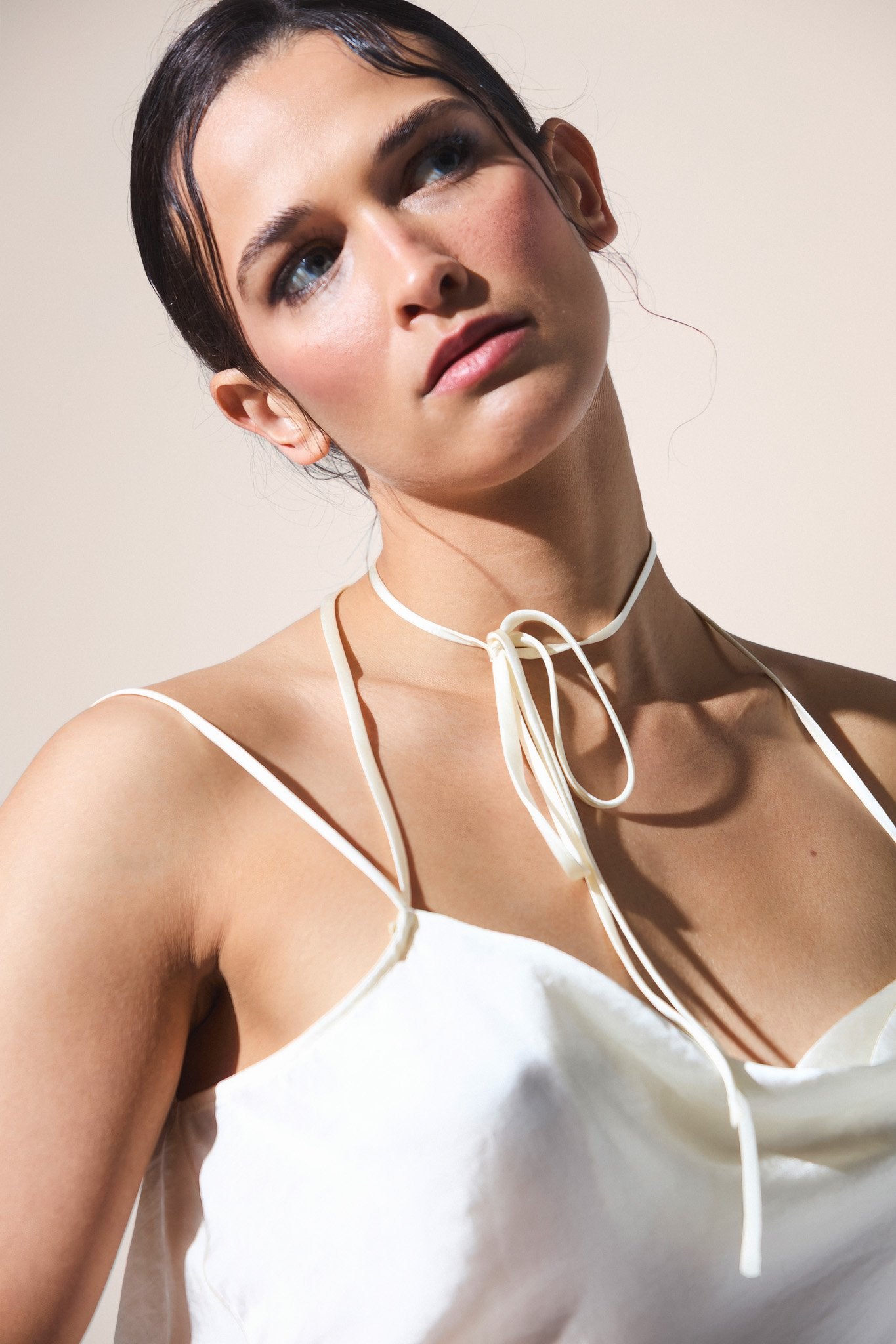 Woman wearing a white top with thin straps and a decorative neck piece against a plain background