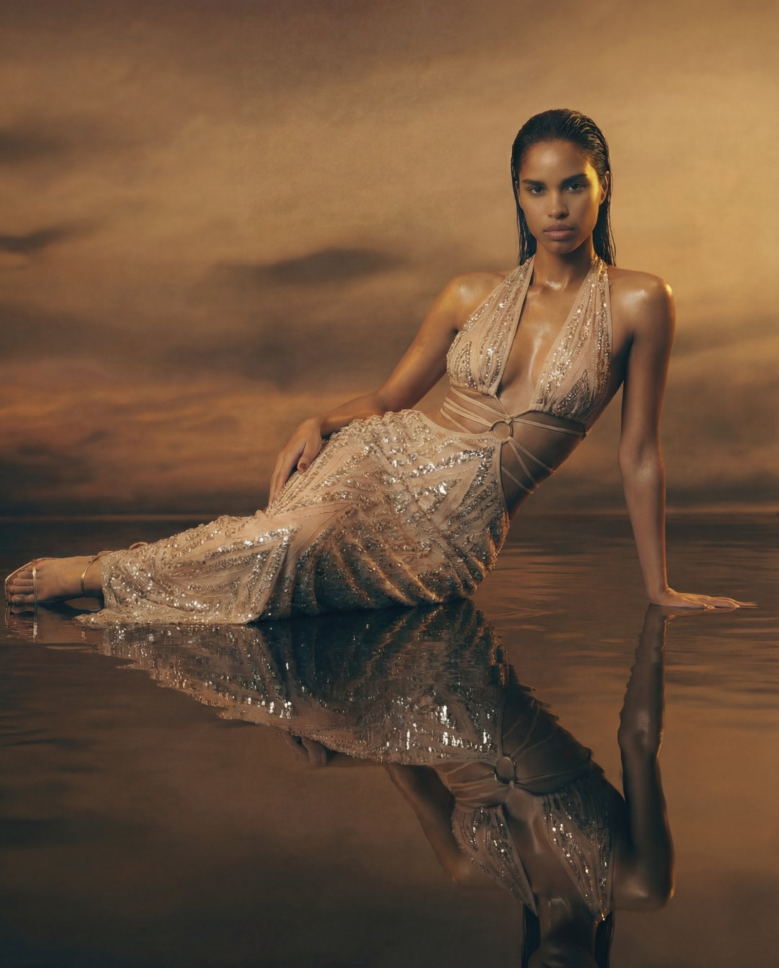 Woman in a sparkling dress sitting in water with a reflective surface