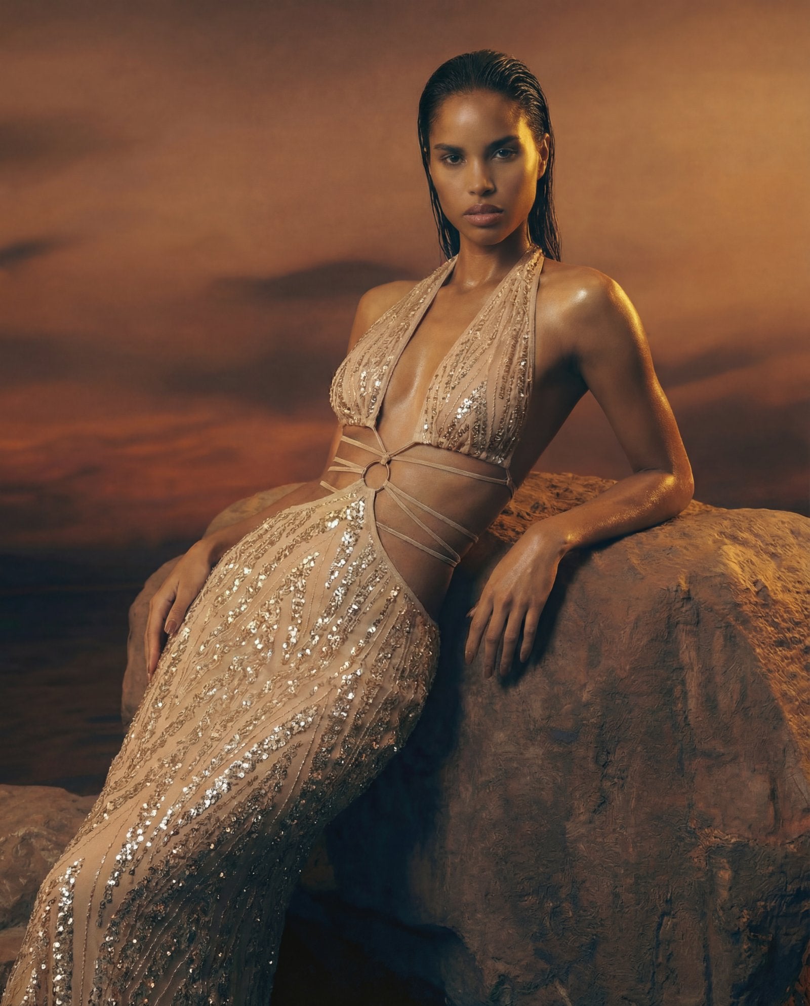 Woman in a sparkling beige outfit sitting on a rock with a desert landscape background