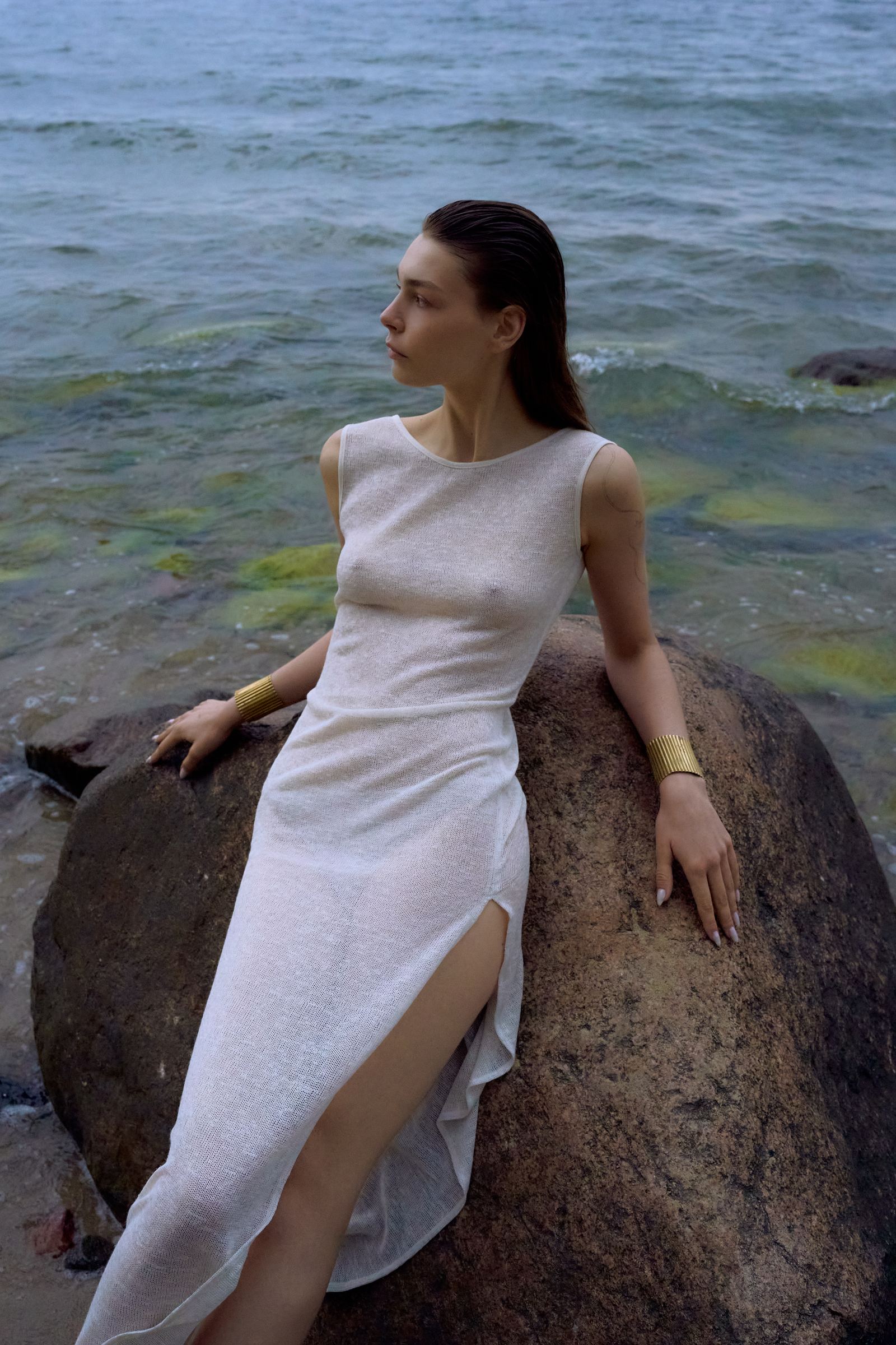 Woman in a white dress sitting on a rock by the sea