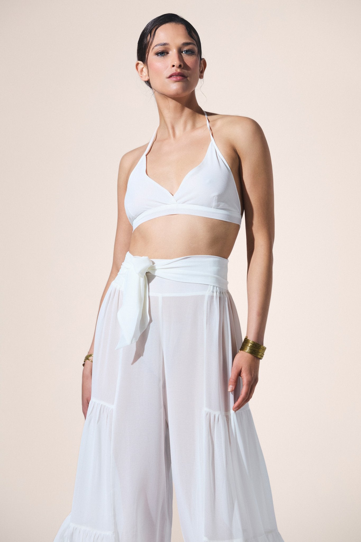 Woman wearing a white bikini top and wide-leg pants against a beige background